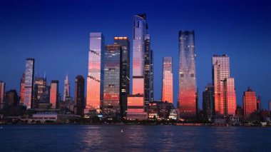 New York, ABD, 8 Temmuz 2025: Göz kamaştırıcı yüksek binalar batan güneşin pembe ışığını yansıtıyor. Gün batımında nehir kenarından New York 'un mimarisine alçak açılı bakış açısı.