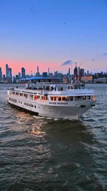 İnsanlar gün batımında yolcu gemisiyle seyahat ederler. Arka planda New York silueti. Dikey video.