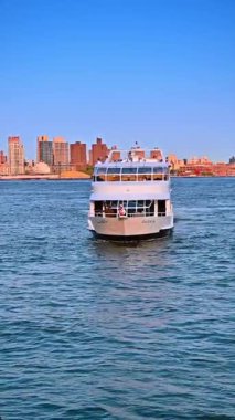 Su manzarasından güzel bir çift güverte yolcu gemisi yaklaşıyor. New York 'un güneşli silueti arka planda. Dikey video.