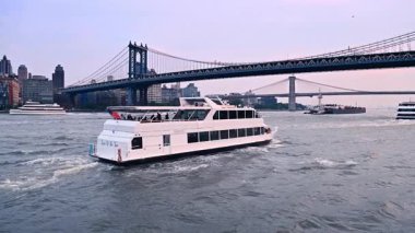 New York, ABD, 8 Temmuz 2025: Çift güverteli tekne Manhattan Köprüsü 'ne doğru nehir kenarından ilerliyor. New York, ABD 'den gün batımında nehir turu.