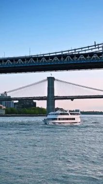 New York, ABD, 8 Temmuz 2025, Manhattan Köprüsü 'nün altından çift güverteli nehir botu geçiyor. Arkaplanda Brooklyn Köprüsü 'nün manzarası. New York nehir turu. Dikey video.