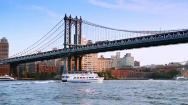Nehir teknesi Manhattan Köprüsü 'nün altından geçiyor. Otobüsler köprüdeki otoyoldan hareket ediyor. New York, ABD.
