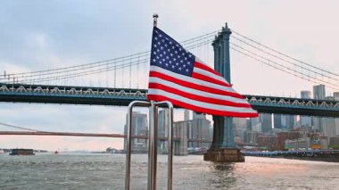 Rüzgarda dalgalanan Amerikan bayrağı metal korkuluklara göre ayarlandı. Manhattan Köprüsü 'nün arka planında alçak açılı görüş.
