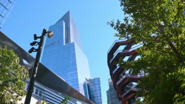 Sokak kameraları, ağaçlar, yüksek binalar ve Taşıyıcı Heykeli olan bir direk. ABD 'nin New York caddesinde alçak görüş açısı.