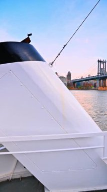 Doğu Nehri 'nde tekne yolculuğu. İki adam gemi güvertesinde geziyor. New York silueti ve Manhattan Köprüsü. Dikey video.