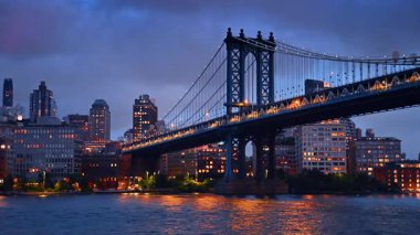 Manhattan Köprüsü ve New York silueti akşamları sokak ışıklarını yakıyor. Nehir manzarasından köprünün alçak açılı görüntüsü.