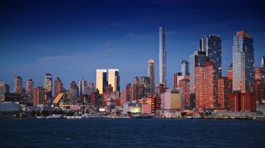Batan güneşin ışığında New York 'un yoğun silueti. Doğu Nehri 'nin koyu mavi sularından şehre bak..
