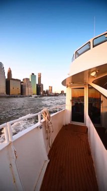 Manhattan Rıhtımı boyunca tekne turu. Manhattan gökdelenleri günbatımını yansıtan bir tekne Doğu Nehri boyunca ilerliyor..