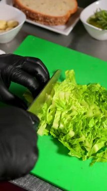 Marulu şeritlere ayırmak. Siyah eldivenli eller kesme tahtasındaki marulları dilimliyor..