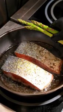 Şef somon tavasına kuşkonmaz ekliyor. Somon filetosu tavada kızarırken el taze kuşkonmaz ekliyor..