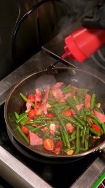 Jambon, fasulye ve domates kızartma tavasında pişiyor. Jambon şeritleri, yeşil fasulyeler, domatesler ve sarımsak soslu bir tavada birlikte pişirilir..