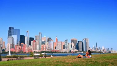 Jersey City, ABD, 11 Temmuz 2025: Manhattan ve Jersey City manzaralı bir parkta dinlenme. Jersey City Parkı 'nda çim üzerinde dinlenen insanlar panoramik Manhattan silueti manzaralı.