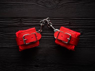 Siyah ahşap arka planda kırmızı kelepçeler. bdsm arkaplanı