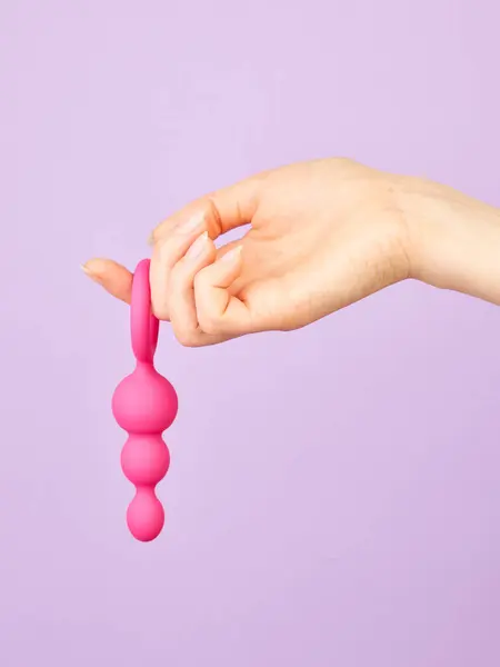 女子的手握住紫色背景的成人性爱玩具 免版税图库照片