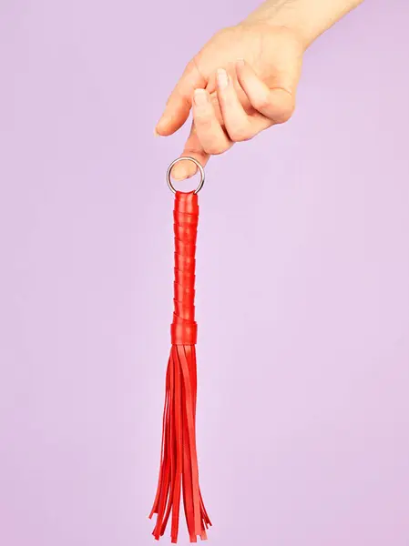 成人角色扮演红鞭游戏在女人手中的紫罗兰色背景 免版税图库图片