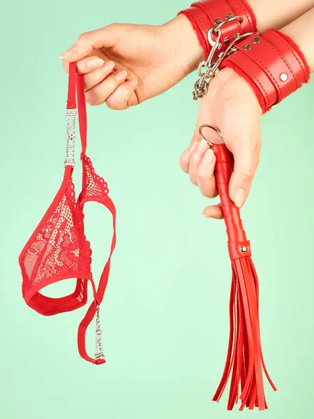 大人の役割のための赤い鞭を保持している女性の手は ミントの背景上のゲームと赤いパンティ ストック写真