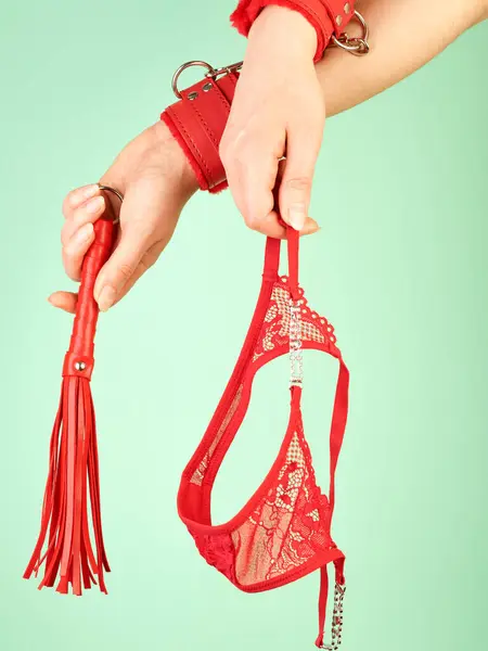 大人の役割のための赤い鞭を保持している女性の手は ミントの背景上のゲームと赤いパンティ ロイヤリティフリーのストック画像