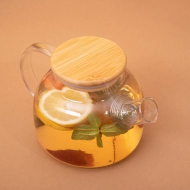 Portakal, böğürtlen ve biberiyeli meyve çayı, cam çaydanlıkta, ahududu tatlısı ve bej arka planda bir fincan ile servis edilir. Meyve çayı. Mevsimlik içki konsepti. Yapılandırma şablonu