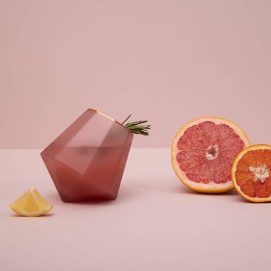 Zarif moda, pembe arka planda narenciye ve biberiyeli pembe altın kokteyl bardağı. Yaz sanatı içecek konsepti