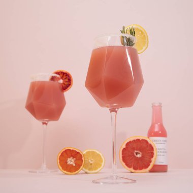 Zarif bir moda ve pembe arka planda narenciye ve biberiye ile süslenmiş şık bir kokteyl. Yaz sanatı içeceği konsepti. Model şablonu