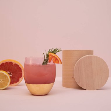 Zarif moda, pembe arka planda narenciye ve biberiyeli pembe altın kokteyl bardağı. Yaz sanatı içeceği konsepti. Ön manzara. Model şablonu