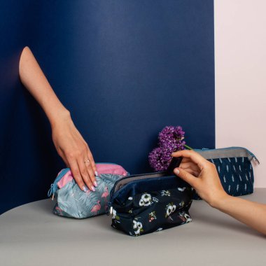 Seyahat Bavulu Seyahat Tuvalet Malzemeleri. Mavi arka planda kadın eli ve kozmetik çantası