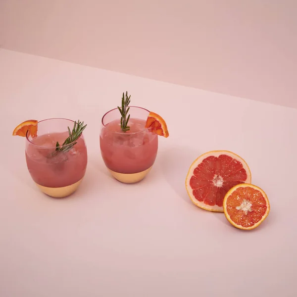 Elegant and trendy pink gold cocktail glasses with citrus fruits and rosemary on a pink background. Summer art food drink concept. Mockup template
