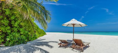 Güzel tropikal güneşli sahil, birkaç güneşli yatak şemsiyesi palmiye yapraklarının altında. Deniz kumu gökyüzü. Romantik rahatlama yaşam tarzı panoramik ada sahili arka planı. Yaz seyahati egzotik tatil manzarası