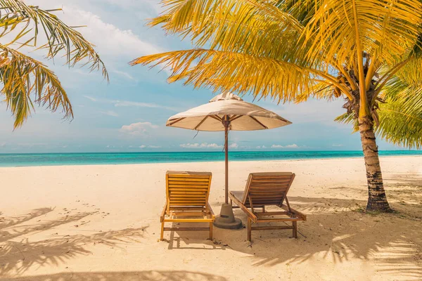Beautiful tropical sunset, couple beds chairs, umbrella under palm tree. Peaceful romantic landscape horizon, golden sky, calm relaxing exotic. Inspirational beach resort. Couples destination scene