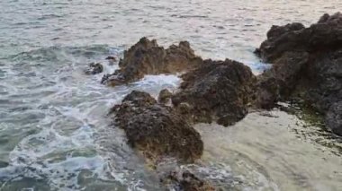 Deniz gün batımında kayalara çarpıyor.