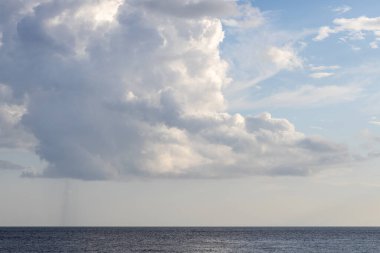 Koyu dramatik bulutlar ve mavi gökyüzündeki güneş ışığı deniz kıyısından yakalıyor.