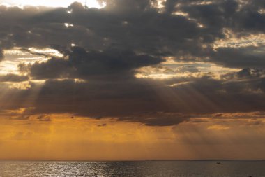 Gün batımında güneş ışığı alan dramatik bulutlar, deniz kıyısından yakalanır.