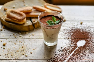 Masadaki şeffaf bardakta tiramisu tatlısı.
