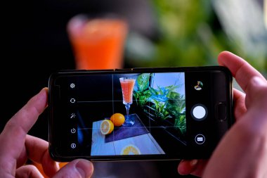 Adam, alkollü bir kokteyl ile akıllı telefonun fotoğrafını çeker. 