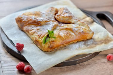 Tüm ahududu turtası ahşap bir tahtanın üzerinde. Masada nane yapraklarıyla süslenmiş.