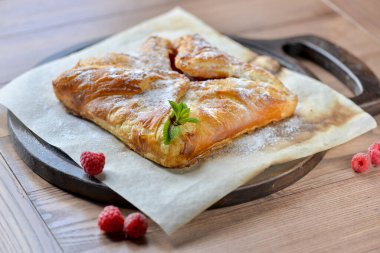 Tüm ahududu turtası ahşap bir tahtanın üzerinde. Masada nane yapraklarıyla süslenmiş.