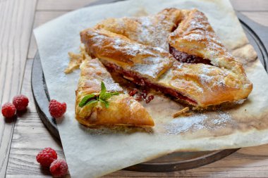 Tüm ahududu turtası ahşap bir tahtanın üzerinde. Masada nane yapraklarıyla süslenmiş.