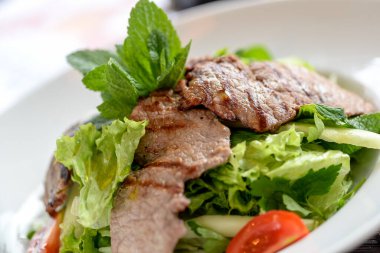 Sebzeli biftek ve arka planda salata.