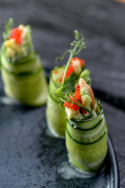 Birkaç rulo taze salatalık ve arka planda kırmızı havyar.