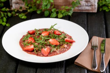 Tabakta taze çilek salatası ve otlar var.