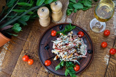 Ahşap bir zeminde, domates ve yeşilliklerle dolu kilden bir tabakta Gürcü sebze salatası.