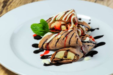 Beyaz tabakta çikolatalı ve muzlu krepler.