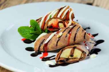 Beyaz tabakta çikolatalı ve muzlu krepler.