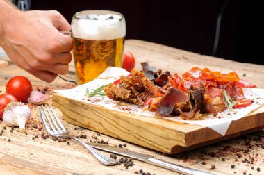 Erkek eli ve tuzlanmış et çeşidi bira aperatifleri bir bardak bira ve ahşap masada biber..