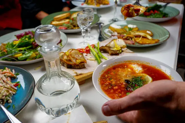 Ukrayna çorbası, domuz yağlı ekmek, salata, patatesli gözleme ve votka olan insanlar.