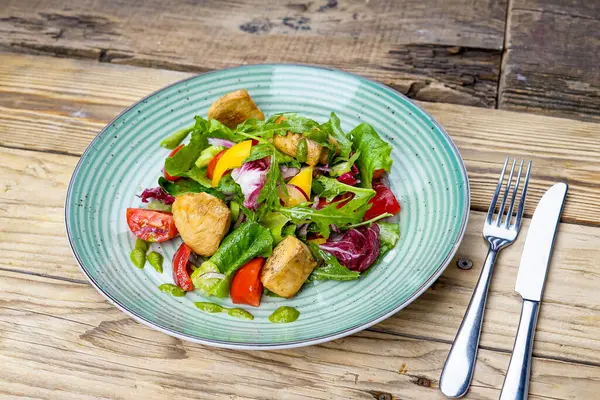 Izgara tavuk filetosu, sebze salatası, çatal ve bıçakla.