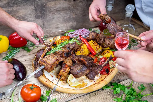Kızarmış etli kebap, sebzeli ve içkili eller.