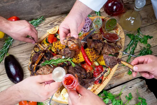 Kızarmış etli kebap, sebzeli ve içkili eller.