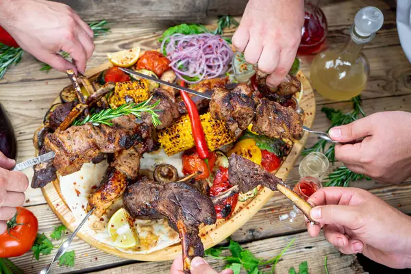 Kızarmış et kebabı, sebze ve alkollü içeceklerle eller.