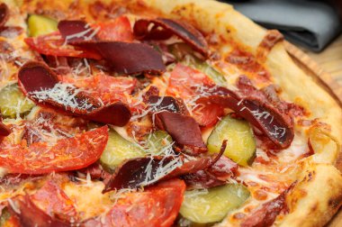 Salamlı lezzetli pizza, salatalık turşusu ve ahşap tahtada jambon.